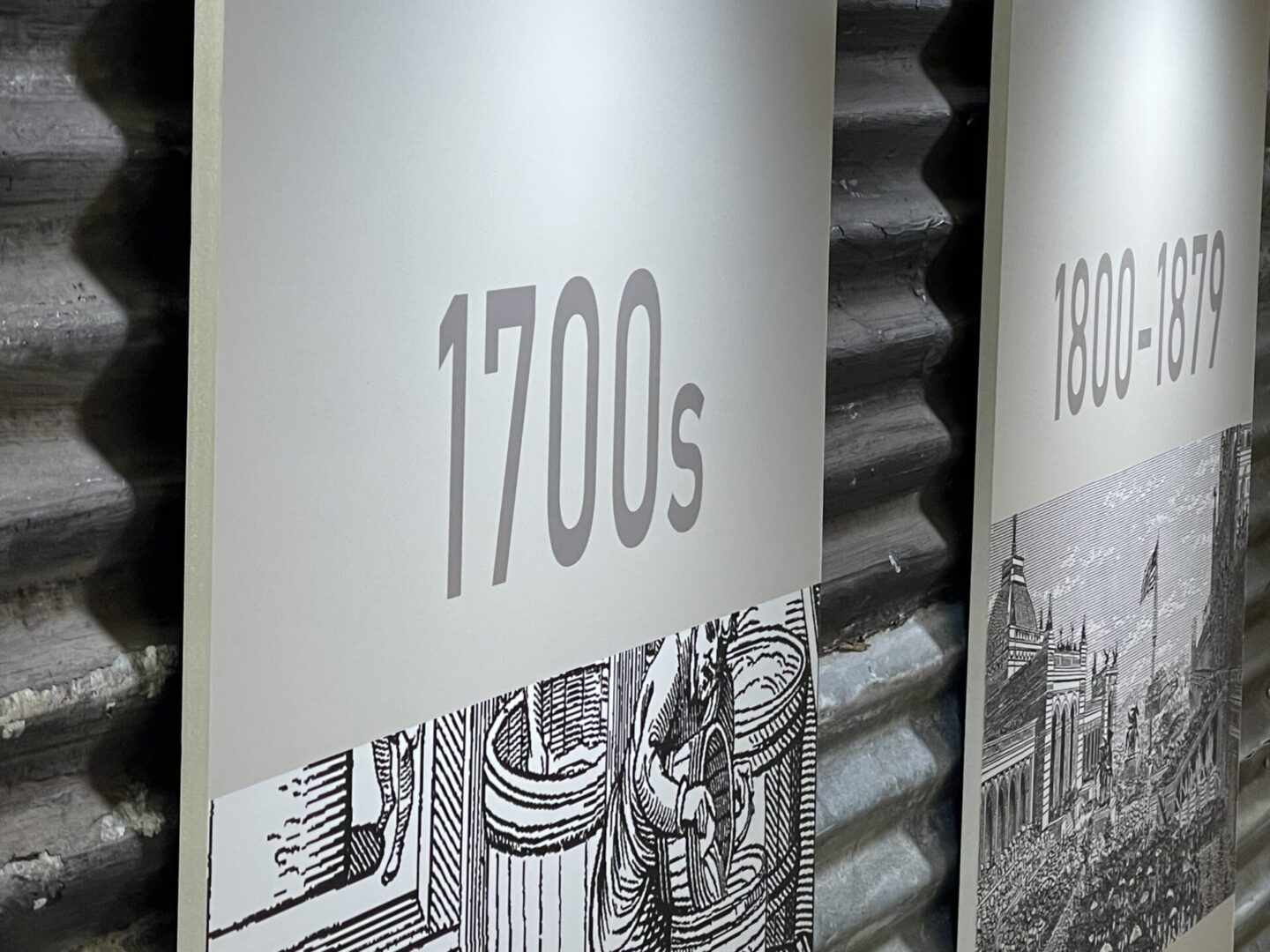 Display panels with illustrations, labeled "1700s" and "1800-1879," against a corrugated metal background.