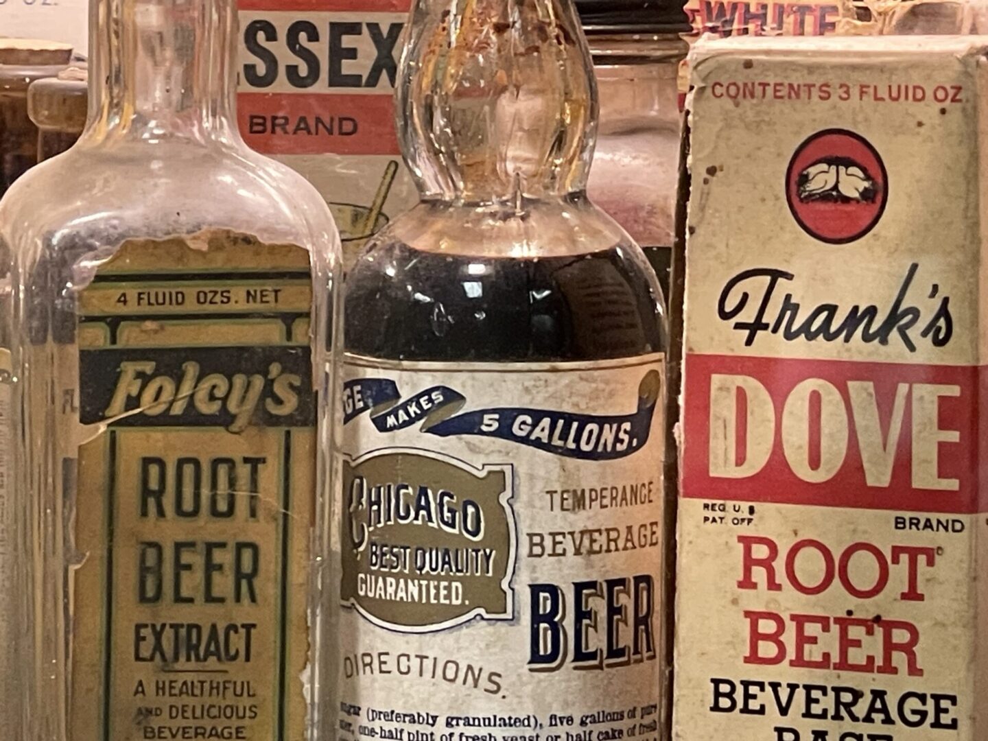 Vintage root beer bottles and packaging on display, including brands like Foley's, Chicago Beverage, and Frank's Dove.