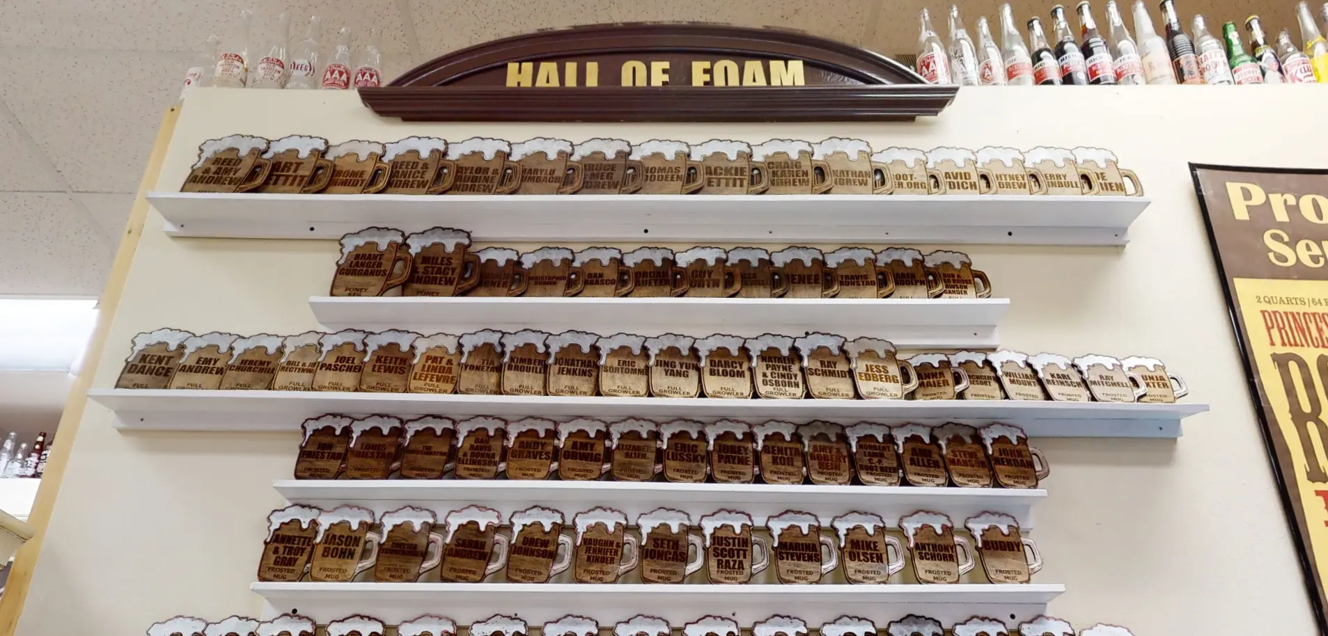 Wall display labeled "Hall of Foam" featuring several rows of wooden plaques shaped like beer mugs.