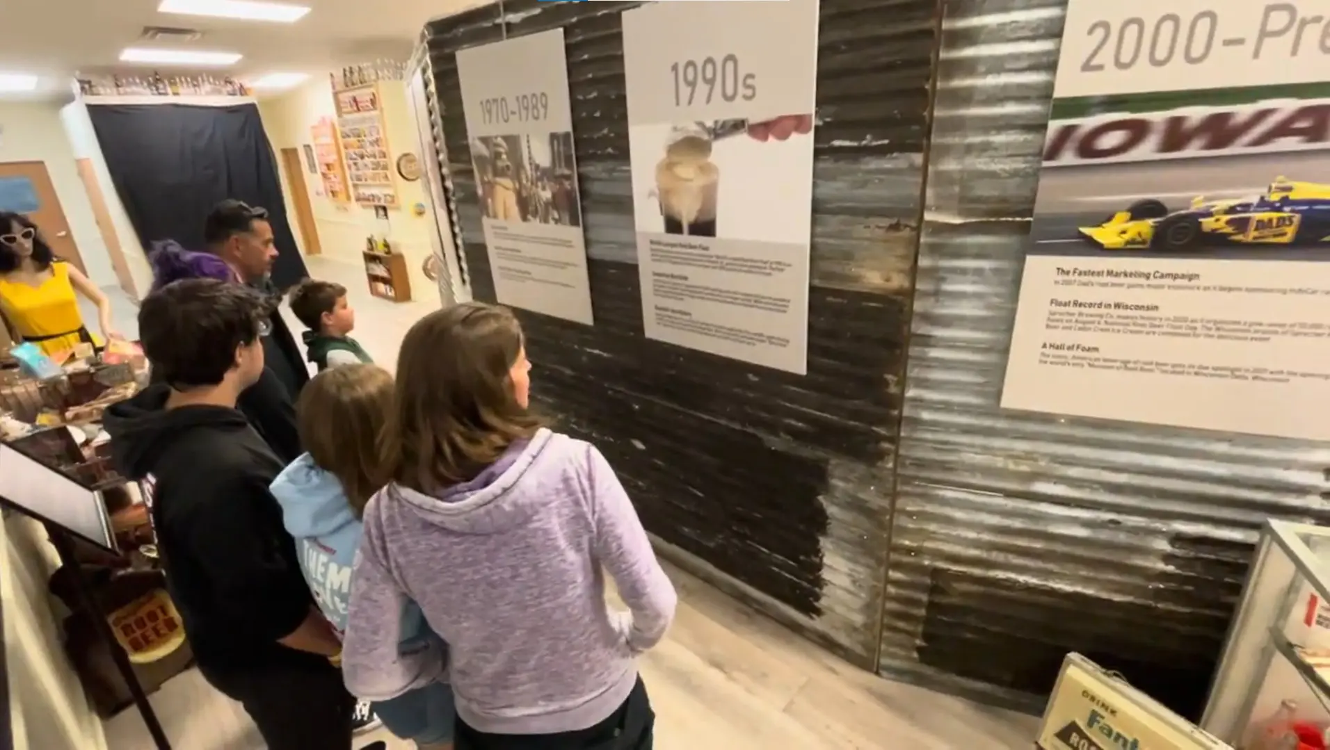 A group of people looking at a museum exhibit displaying historical information on a corrugated metal wall.