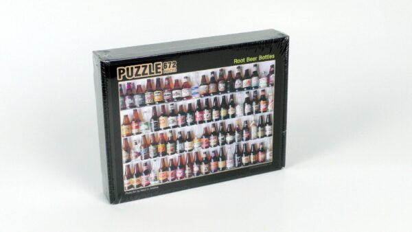 The Root Beer Bottles Puzzle, a sealed jigsaw box, features an image that brings to mind a beer museum, displaying an array of root beer bottles on shelves. With "672 Pieces" clearly labeled, this delightful challenge is perfect for enthusiasts and collectors alike.