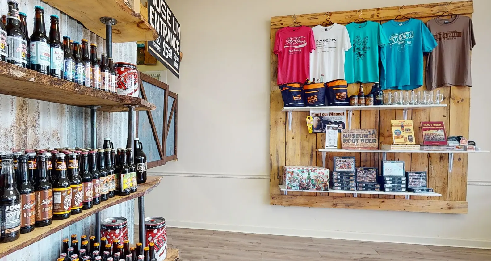 Store interior with shelves displaying various bottled beverages on the left, and merchandise like t-shirts and mugs on a wooden wall display on the right.